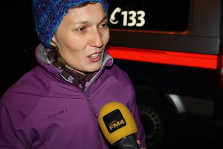 Grünen-Gemeinderätin Martina Wurzer im Interview von FM4 mit lila Jacke vor einem Polizeiwagen